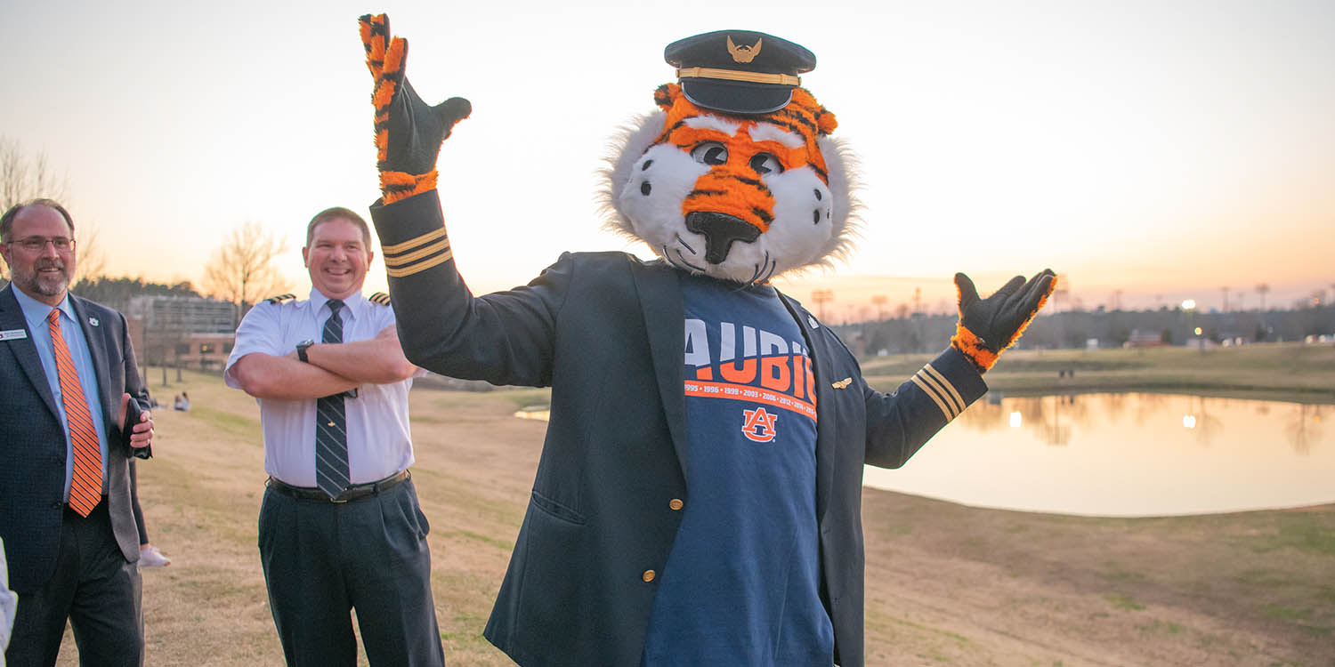 Auburn university mascot posing for picture with arms in air and instructors standing behind