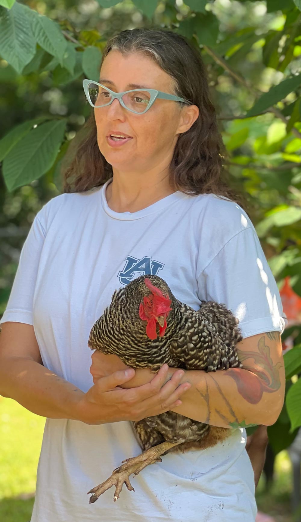 Becki Ratzlaff holding chicken with trees behind