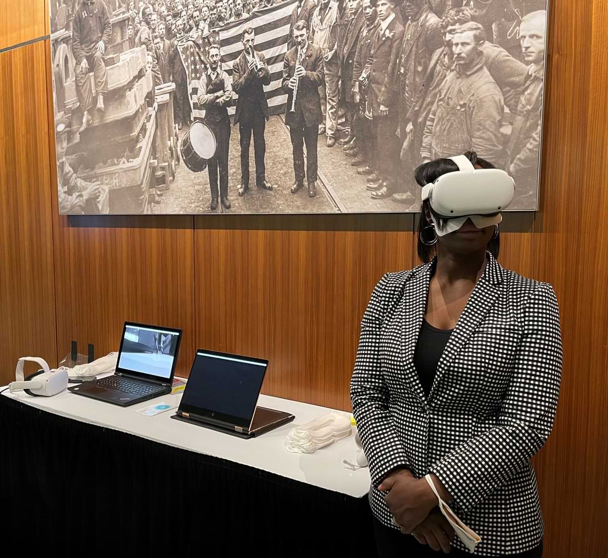 Professor wearing VR headset to demonstrate an immersive experience with large photograph of marchers in background