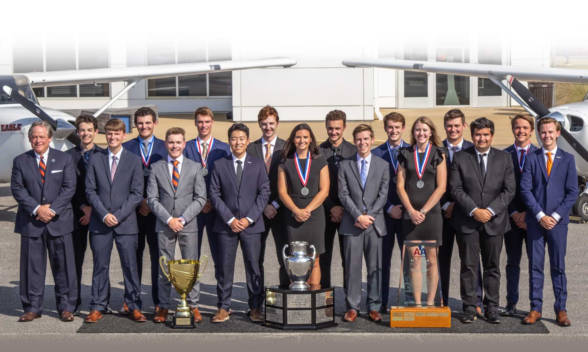 Aviation students and instructors group photo in front of trophies