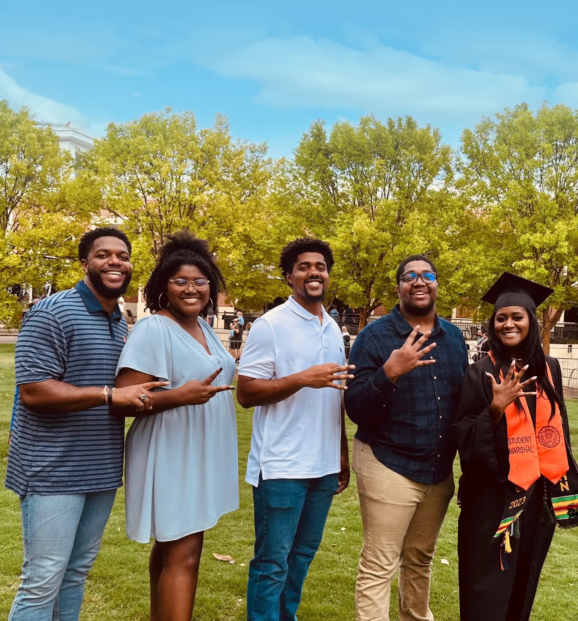Harlan, Kayla, Jakobi, Jordan and Diani Bailey holding up fingers for which number sibling they are and went to Auburn with blue sky and trees in background