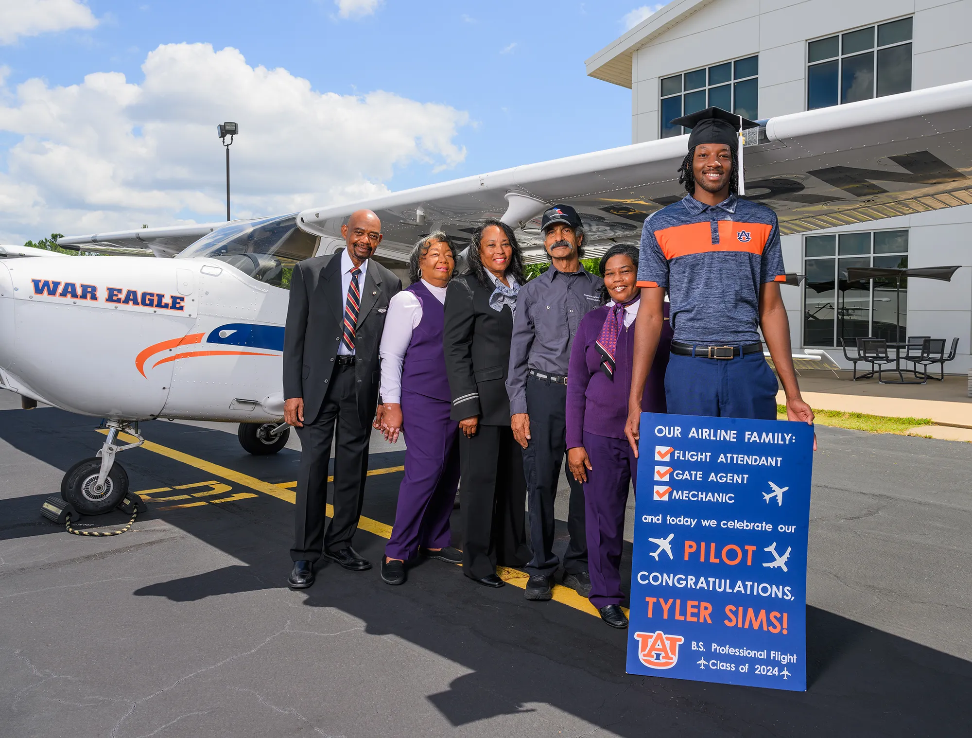 Tyler wearing graduation cap standing with family by Auburn plane