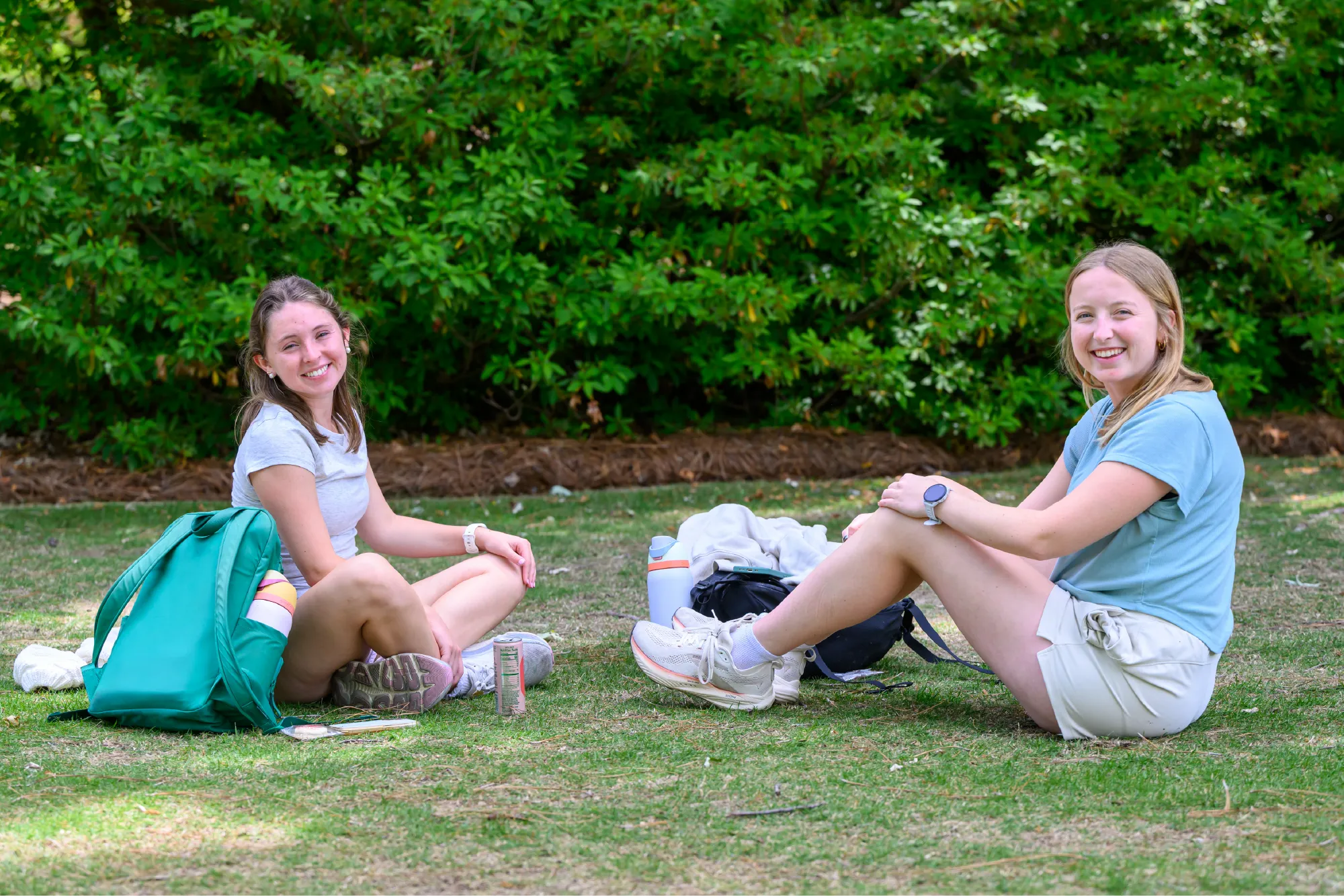 Two Auburn University students smiling while sitting on the grass with backpacks and water bottles nearby.
